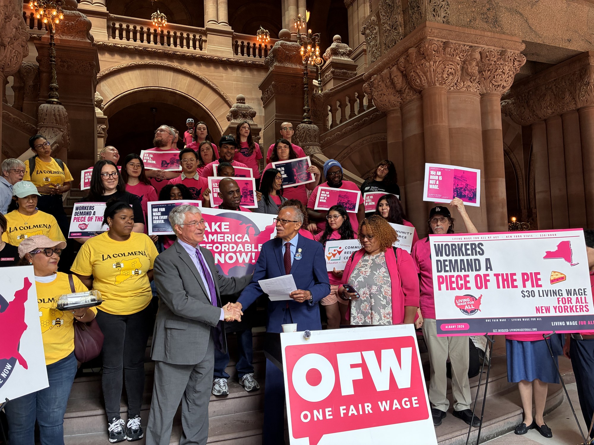 Sen. Robert Jackson and Asm. Phil Steck shake hands on the Million-Dollar Staircase at the New York State Capitol, with the Living Wage For All NY Coalition behind them